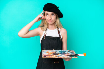 Young artist caucasian woman holding a palette isolated on blue background having doubts and...