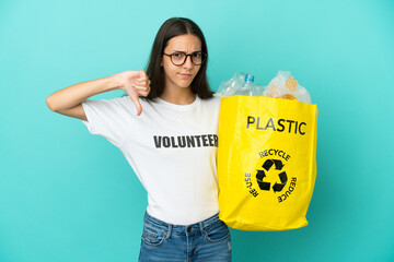 Young French girl holding a bag full of plastic bottles to recycle showing thumb down with negative...