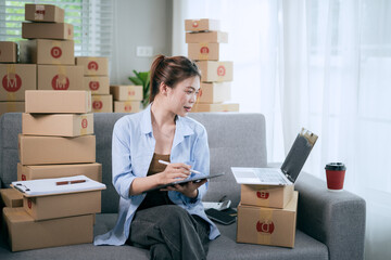 An Asian woman uses a tablet to manage online orders and prepare packages for shipping — reflecting the growth of SME businesses and the rising trend of online shopping.