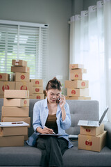 An Asian woman uses a tablet to manage online orders and prepare packages for shipping — reflecting the growth of SME businesses and the rising trend of online shopping.