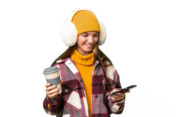 Teenager caucasian girl wearing winter muffs over isolated background holding coffee to take away...