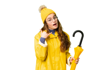 Teenager girl with rainproof coat and umbrella over isolated chroma key background making phone gesture. Call me back sign