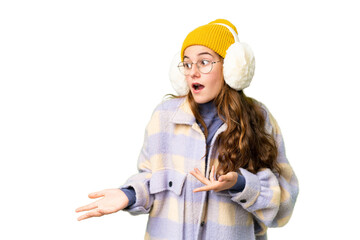 Teenager girl wearing winter muffs over isolated chroma key background with surprise facial expression