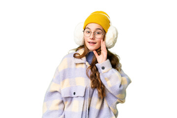 Teenager girl wearing winter muffs over isolated chroma key background shouting with mouth wide open