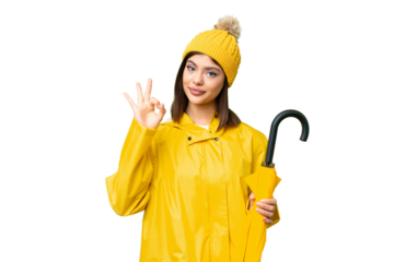Young Russian woman with rainproof coat and umbrella over isolated chroma key background showing ok sign with fingers