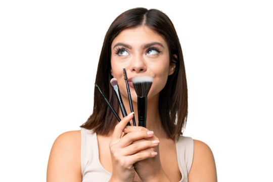 Young Russian woman with rainproof coat and umbrella over isolated chroma key background holding makeup brush and looking up