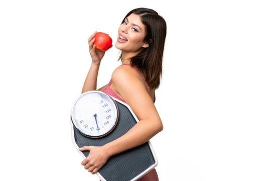 Young Russian woman with rainproof coat and umbrella over isolated chroma key background with weighing machine and with an apple