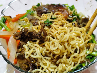 Beef noodle soup is equipped with various delicious toppings served in a glass bowl.