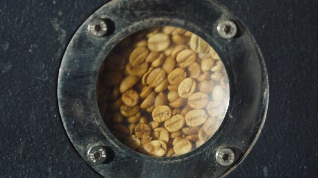 Raw green coffee beans rotating inside industrial roasting machine, transforming from verdant seeds to aromatic roasted product during initial manufacturing stage