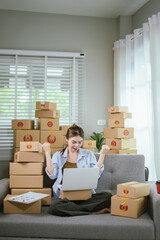 An Asian female entrepreneur is preparing parcels and checking online orders of her products to ship to customers using a laptop at home. A concept of online shopping and a small startup SME business.