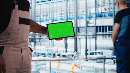 Smart factory engineer oversees operation of robotic arms and conveyor belts using green screen...