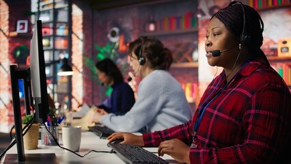 Happy call center agent providing step by step guidance to customers. Smiling customer center worker at PC desk walking clients through technical solutions during call, camera B
