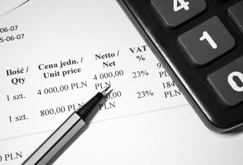 A pen lying on a paper VAT invoice next to a calculator,