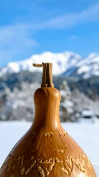 Close-up of a tan gourd with an etched pine tree landscape on a snow covered background, featuring bright blue sky and distant mountains