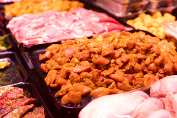 Marinated chicken pieces in curry are displayed in display case. Butcher shop sells fresh meat products, semi-finished products