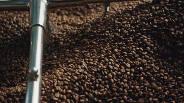 Rotating mechanical arm mixing freshly roasted coffee beans inside industrial roasting equipment, showcasing precision of coffee production process