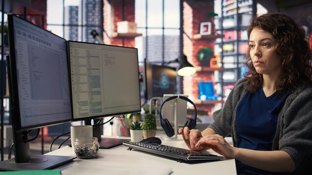 Young woman at the office looking at UI on PC display and executing binary code for testing and implementing something on the software. Coding application for computer science. Camera A.