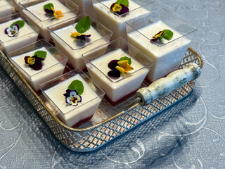 Mini panna cotta desserts with blended fruit layer, mint leaves, and edible flowers. Served in...