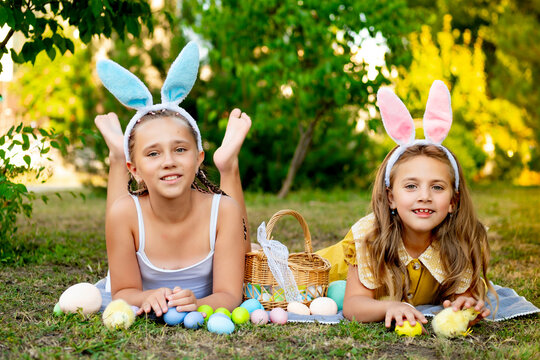 Easter, children play with Easter eggs in bunny ears on the green lawn. Easter tradition. Children with a basket full of colorful eggs - Powered by Adobe
