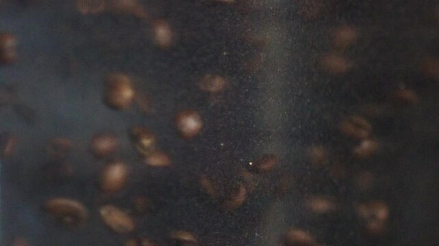 Rotating brown coffee beans transforming inside industrial coffee roasting equipment, revealing complex roasting stages and developing rich aromatic characteristics during production process