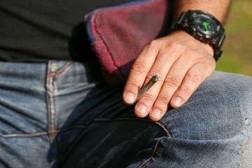 A man's hand holding a lit rolling cigarette or joint, copy space