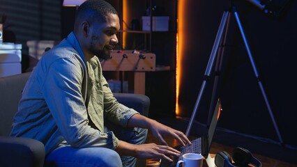 Young black adult working on his freelance tasks in the living room, adjusting his job schedule and...