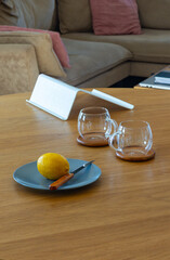 Still life composition with fresh lemon, knife, and empty glass cups on a wooden table in cozy kitchen environment. Side view with natural lighting