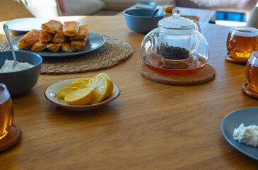 Glass teacup with lemon, sweet rolls, and cottage cheese on rustic wooden table in a bright living...