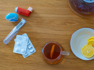 Top view of home remedy setup with teapot, hot tea, citrus, pills, thermometer and asthma inhaler on wooden surface. Concept of health recovery and immune support