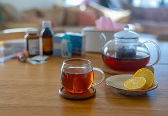 Warm herbal tea with lemon on a wooden table with cold medicine and tissue box in background....