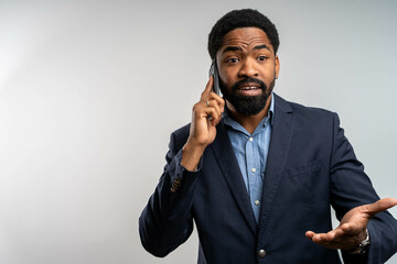 Young Black businessman in suit making worried phone call, isolated on white background, stressed...