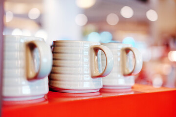 A row of ribbed mugs sits on an orange display, with a blurred retail background suggesting a...