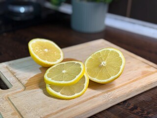 A ripe yellow lemon cut into halves and slices lies on a wooden cutting board in a kitchen. Bright...