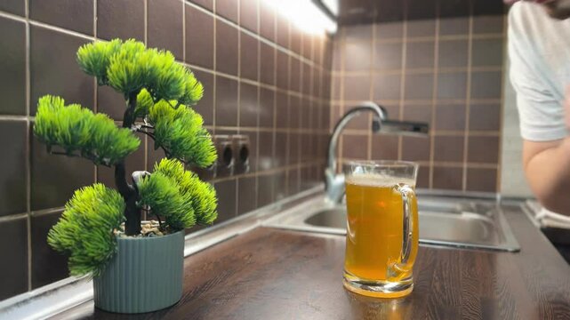 A man smells a jar of homemade kombucha covered with gauze on a kitchen counter. The tea fungus is forming inside, emitting a strong sour aroma.