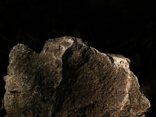 Dramatic close-up of a textured stone illuminated by low sunlight against a dark background. Abstract natural form with rich detail and contrast