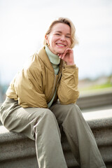Smiling mature blond woman sitting outdoors in casual winter clothing