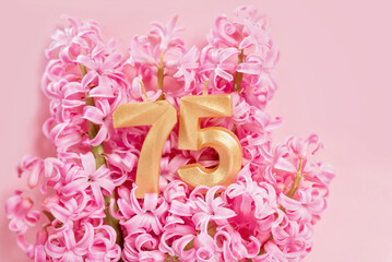 Number 75 seventy five golden celebration birthday candle on Pink flowers Background. 75 years birthday. concept of celebrating birthday, anniversary, important date, holiday milestone