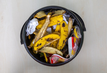 Black bucket filled with various household waste. Includes food scraps, paper, plastic. Top view of...