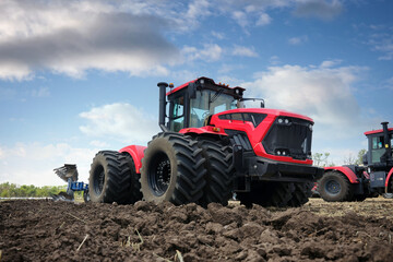 Close-up of a plowed field. In the background are large modern tractors red color with a plow.