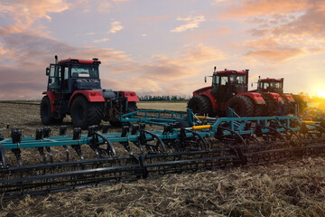 Several large tractors stand in a field against the backdrop of a sunset sky.