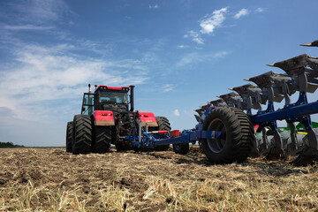 Rear view of a large tractor work with a plow in a field. Start tillage after harvest.
