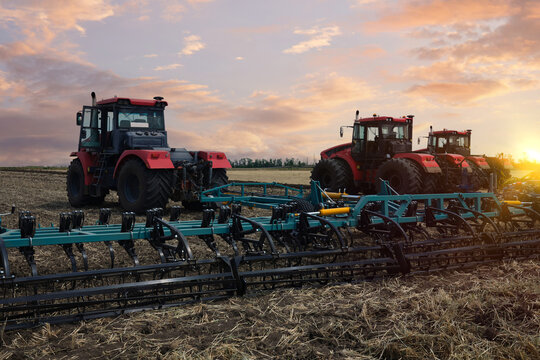 Several large tractors stand in a field against the backdrop of a sunset sky.