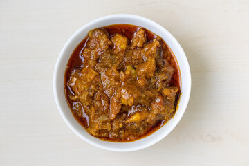 Delicious beef bhuna curry in white bowl on wooden surface, top view. Flavorful Bengali dish, authentic traditional Asian food, spicy aromatic meal.