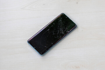 Smartphone with cracked screen on wooden background. Damaged mobile phone, broken display.