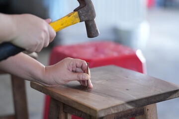 a person using a hammer to drive a nail into a wooden surface, with one hand holding the nail and the other gripping the hammer. This scene represents woodworking or DIY repair work