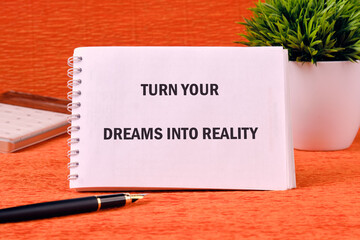 TURN YOUR DREAMS INTO REALITY words on a spiral notebook on an orange background