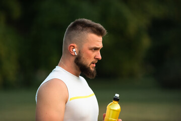 A young, fit man listens to music on wireless headphones and relaxes after a run or workout in a...