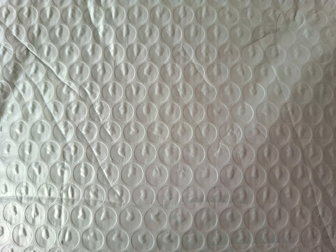 Bubble wrap texture with circular patterns of translucent plastic, featuring wrinkles and creases. The surface catches light, creating subtle reflections and shadows on each bubble
