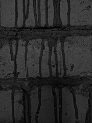 Dark, textured brick wall with vertical streaks of dripping black liquid. Rough surface and irregular patterns create a gritty, urban, and mysterious atmosphere. No visible text