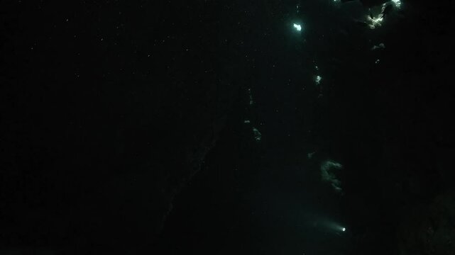 A scuba diver slowly advances in a pitch-black marine cave, guided only by a narrow beam of torchlight. Check my portfolio for more cave diving footage.